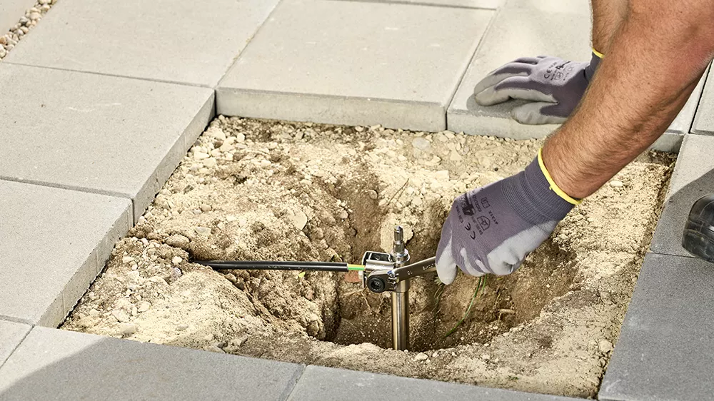 A man digs a hole in the ground using a tool to install a deep earth electrode.