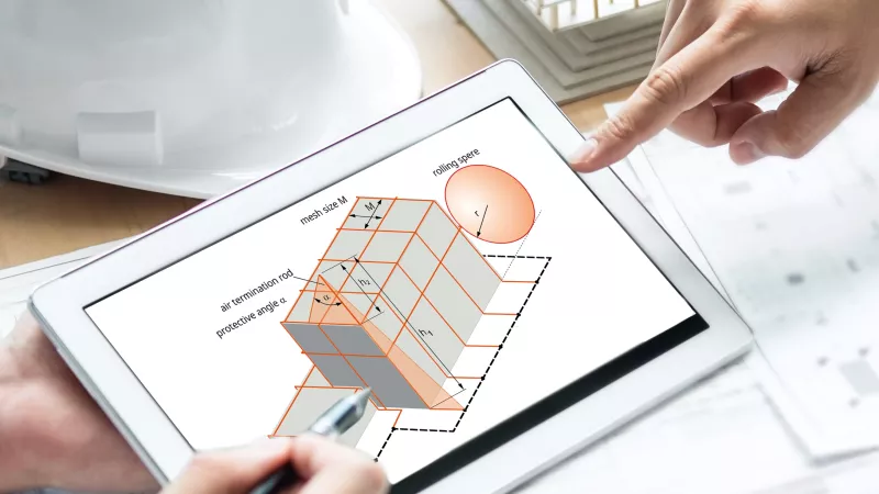 Hands pointing at a 3D architectural model displayed on a tablet, with a white construction helmet and a calculator on the table.