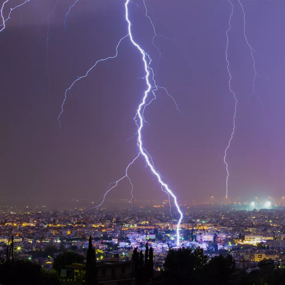 A bright lightning bolt striking a city at night, illuminating buildings under a purple sky.