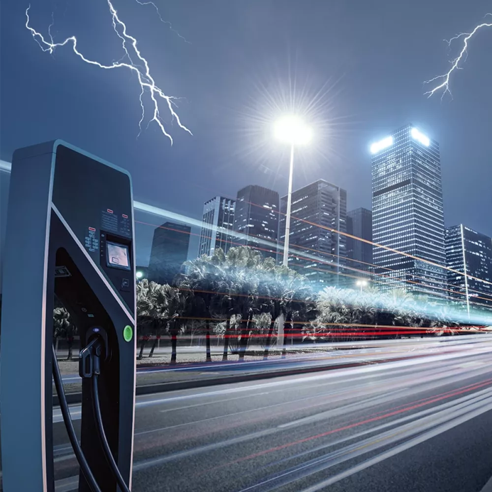 Electric vehicle charging station and power cabinet in an urban setting at night, with lightning over a city skyline.