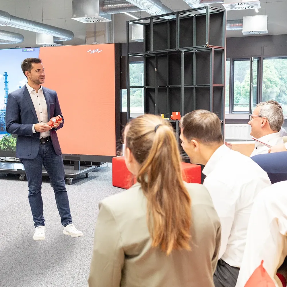 Man presenting device to seated group in training room with large display screen