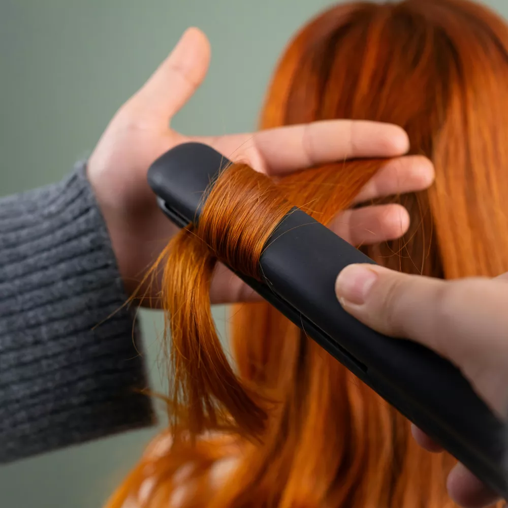 una donna dalla chioma fulva usa una piastra per capelli