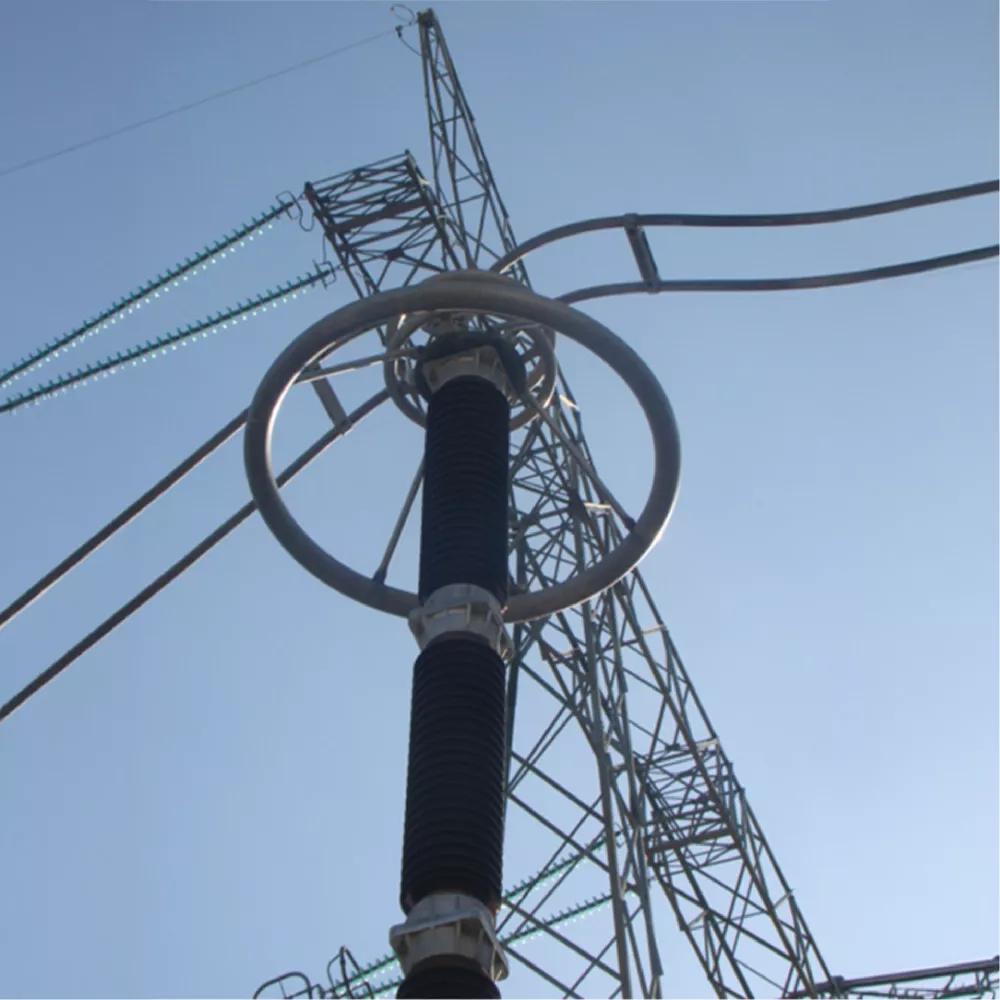 Close-up view of a high-voltage electrical component and transmission tower against a clear sky.