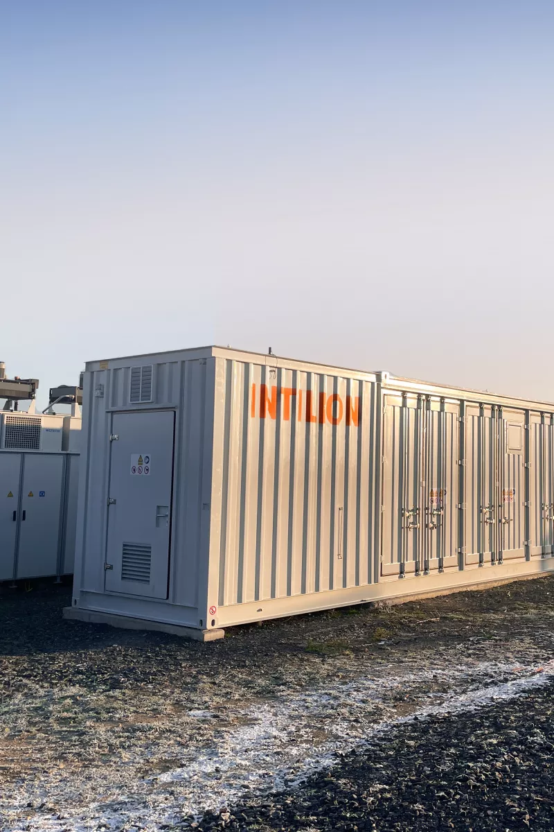 Large, light gray, modular containerized power equipment, labeled INTILION, situated amongst solar panels.