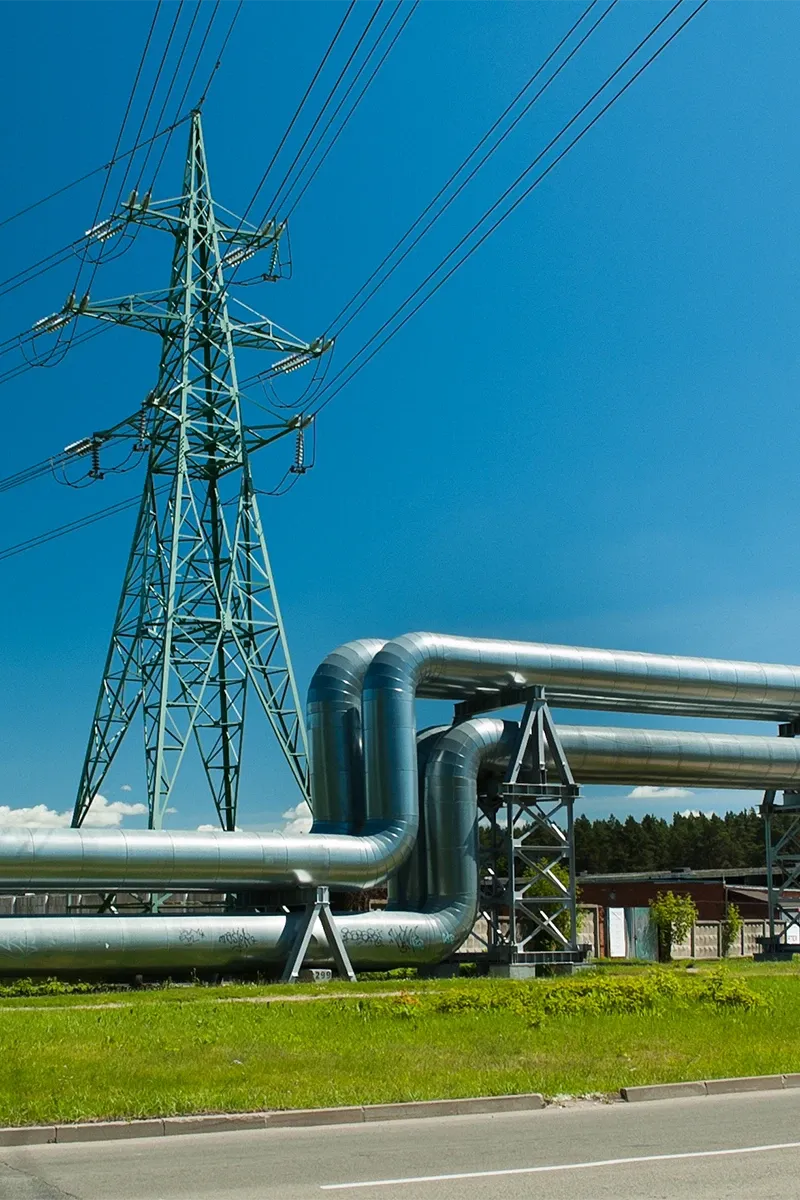 Grande traliccio elettrico verde dietro a una pipeline su un prato sotto un cielo azzurro.