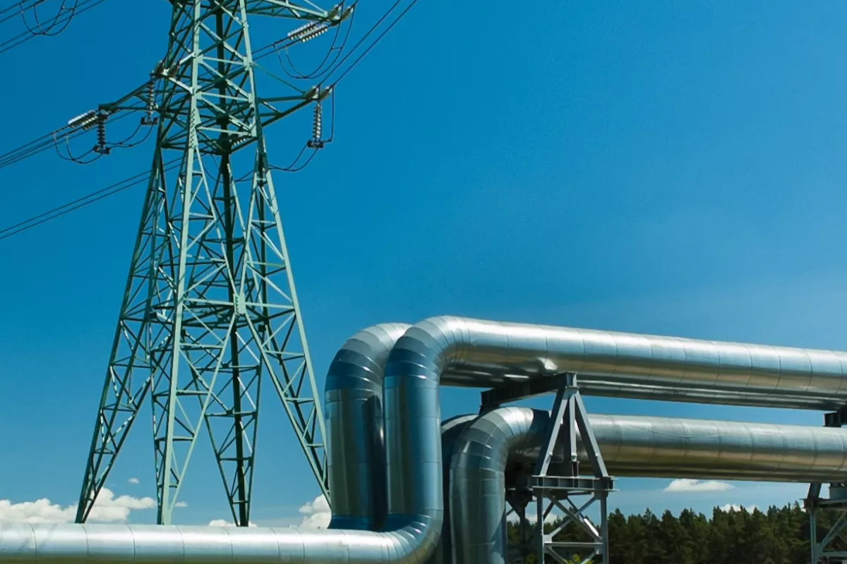 Linea ad alta tensione e conduttura su prato verde con cielo blu.