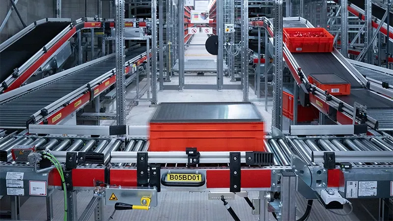 Automatisiertes Fördersystem mit roten Behältern in Lagerumgebung.